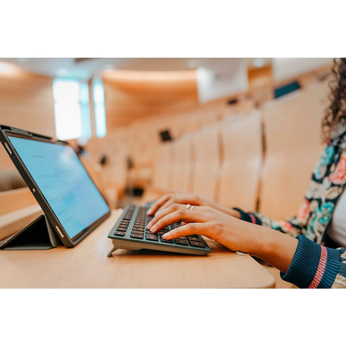 Personne tapant sur un clavier. Devant elle, une tablette dans un amphithéâtre.