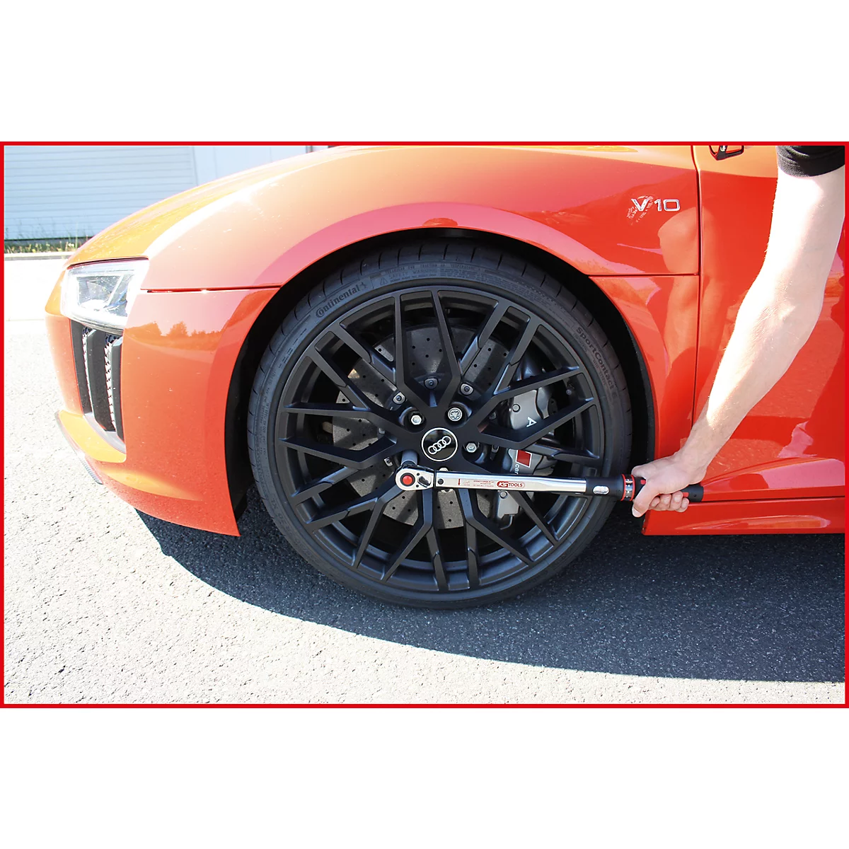 Gros plan d'une voiture rouge, un homme serre les écrous de roue avec une clé dynamométrique.