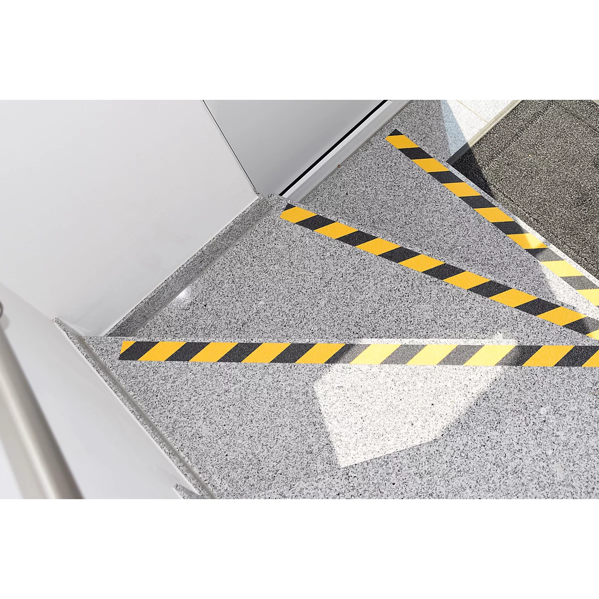Staircase with yellow and black warning stripes, grey floor, light wall. The warning stripes mark the edges of the stairs.