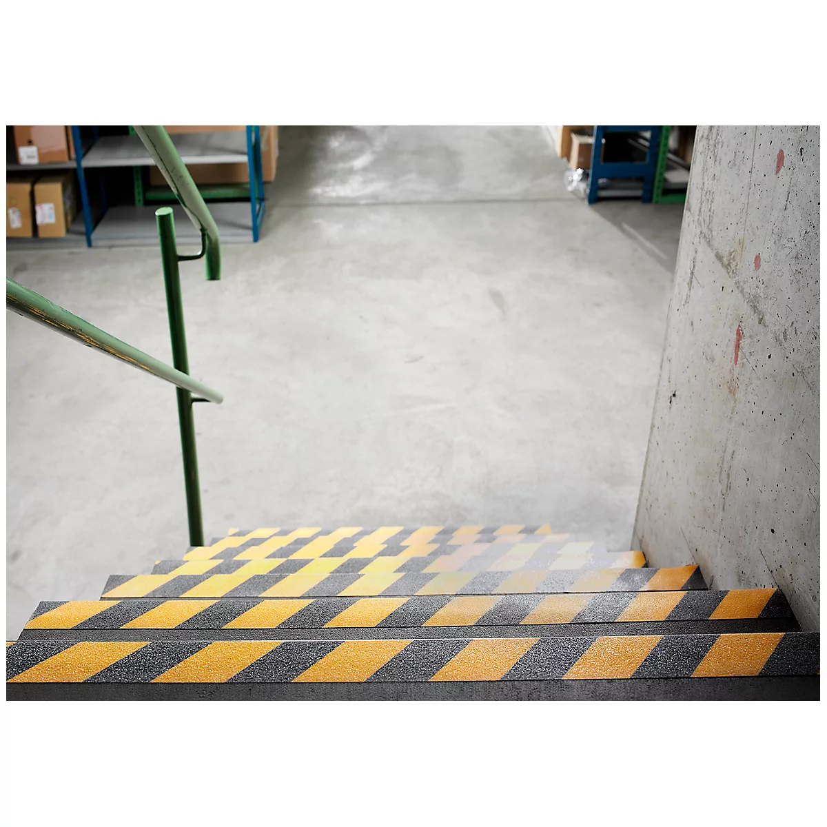 Stairs with yellow and black warning stripes and a green handrail. Concrete wall on the right.