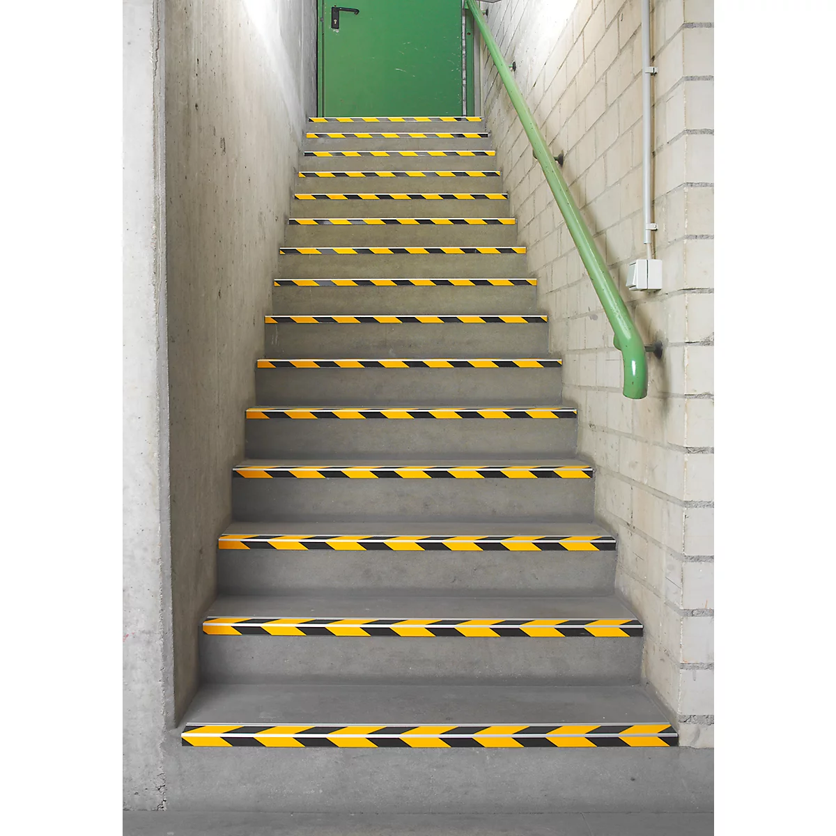 Staircase with yellow and black warning stripes, green handrail, green door.