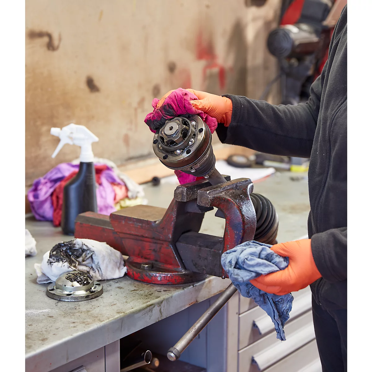 Mechanic cleaning a car part in a workshop, wearing gloves and using cloths.