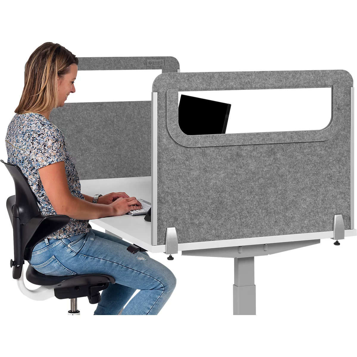 Femme assise à un bureau avec une cloison et tapant sur un ordinateur portable. Mur gris, bureau blanc, chaise de bureau noire.