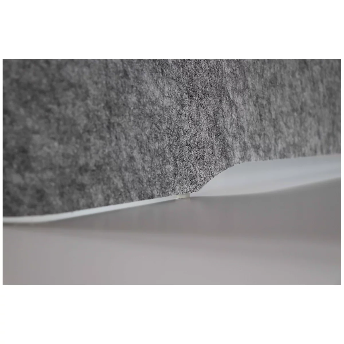 Le tissu en feutre gris rencontre une surface en plastique claire et ondulée. Le contraste de texture et de forme est évident.