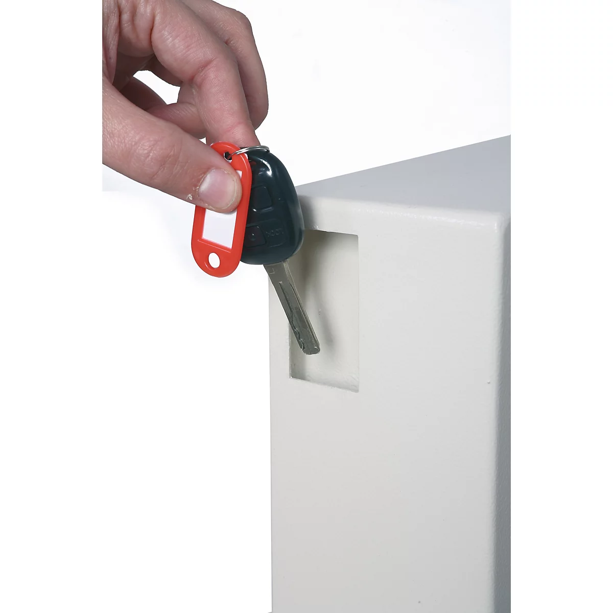 Une main insère une clé avec un porte-clés rouge dans la fente d'un boîtier métallique clair.