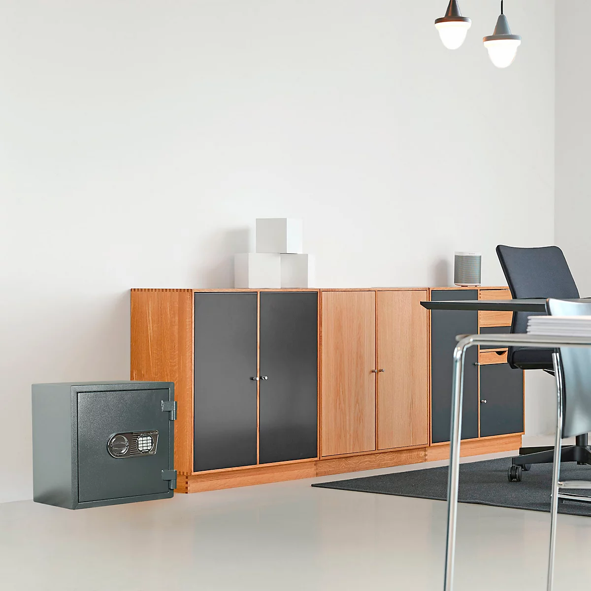 Coffre-fort gris dans un bureau, à côté d'un mur d'armoires en bois, d'un bureau et d'une chaise.