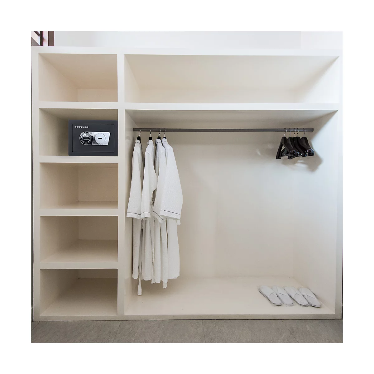 Un placard blanc vide avec des peignoirs, un coffre-fort et des pantoufles. La tringle à vêtements contient des peignoirs et des cintres.