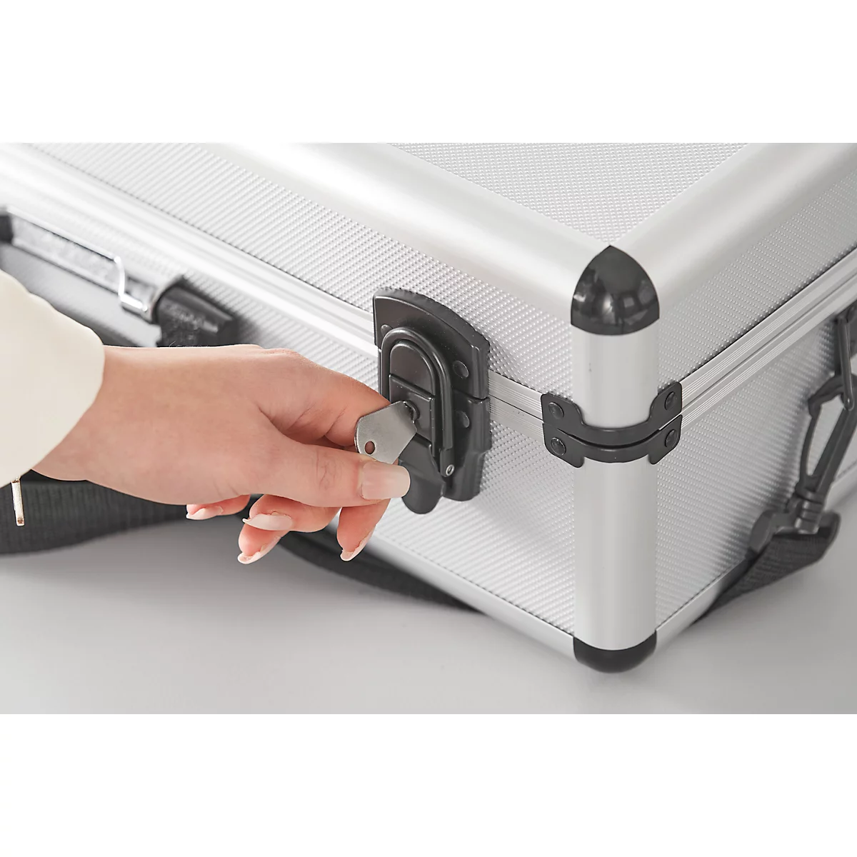 Une main verrouille une valise argentée avec une clé.