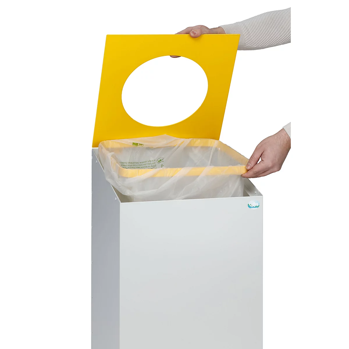 Une personne soulève un couvercle jaune avec un trou pour accéder à un sac poubelle à l'intérieur d'une poubelle blanche.