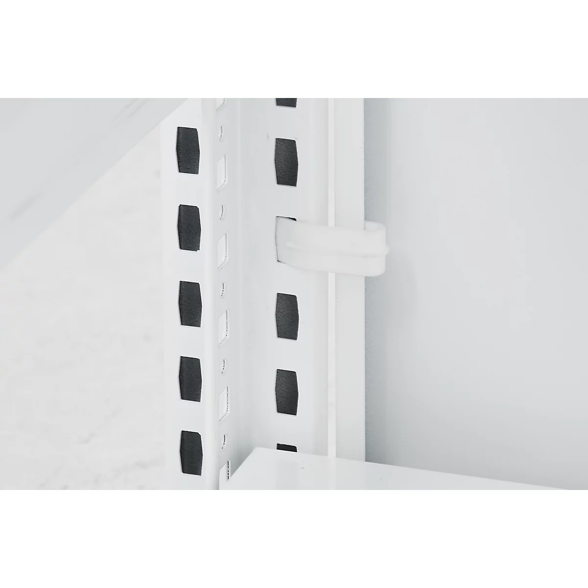 Gros plan d'une équerre d'étagère blanche avec des trous noirs et un clip de maintien blanc.