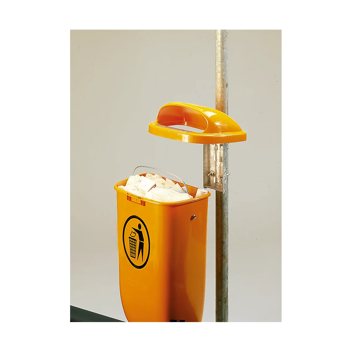 Yellow trash can with lid, attached to metal pole. Trash can is full of paper. Sticker with trash symbol.