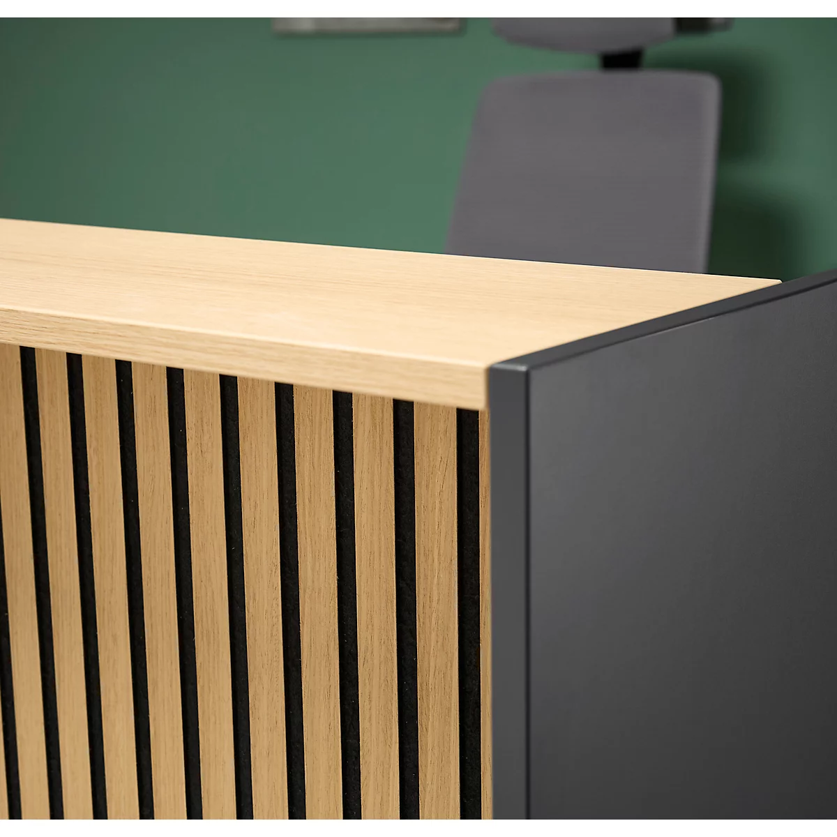 Gros plan d'une réception en bois avec des rayures noires verticales et un panneau latéral noir. Une chaise de bureau et un mur vert sont visibles en arrière-plan.