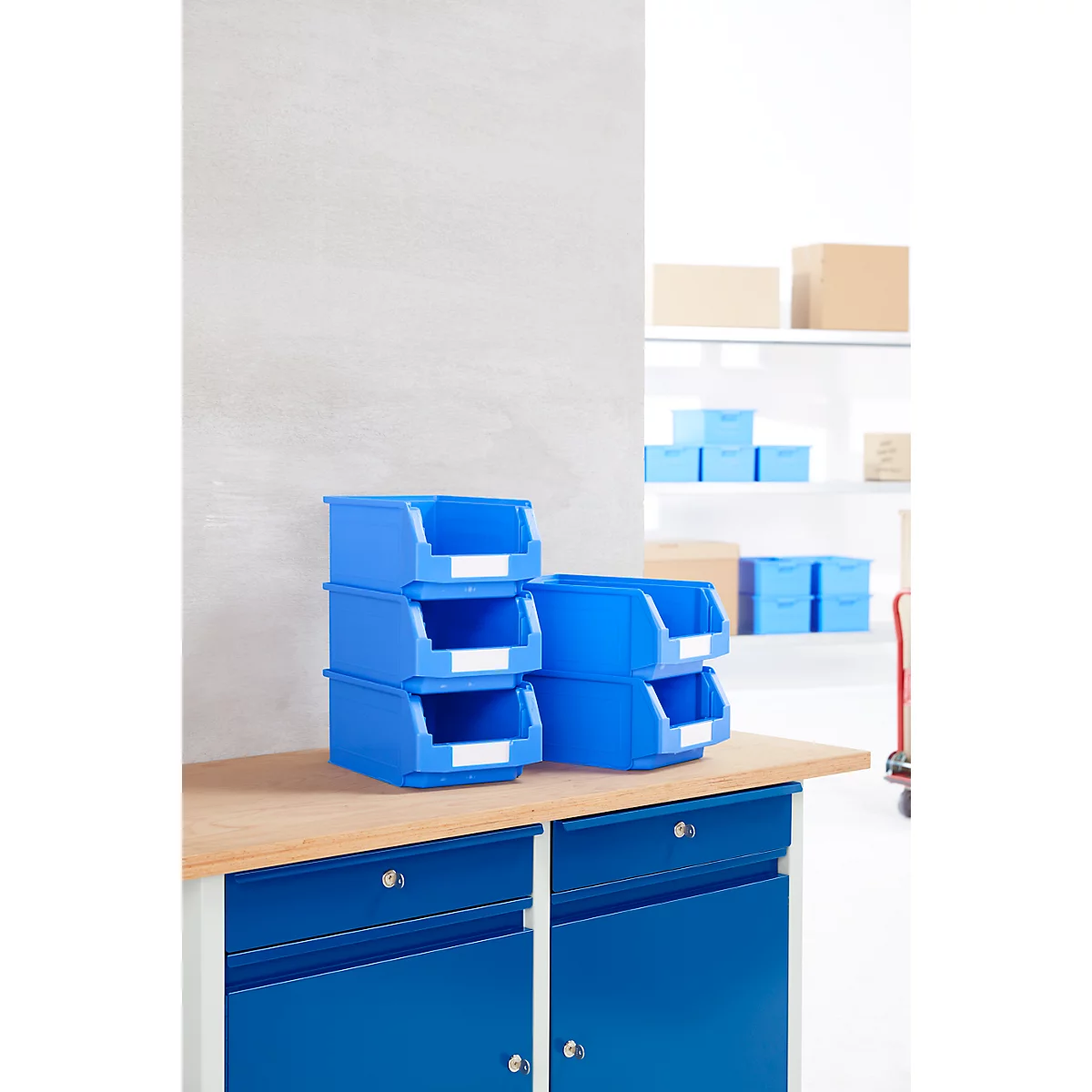 Cajas de almacenamiento azules sobre un banco de trabajo. En el fondo hay más cajas y una estantería.