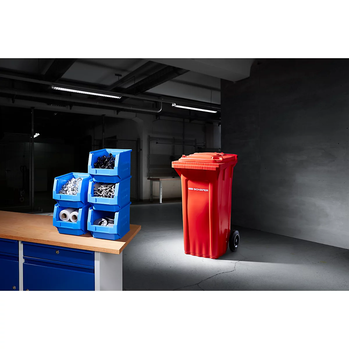 Contenedores azules con herramientas y un contenedor de basura rojo en un taller. En el contenedor pone "eliminación de residuos".