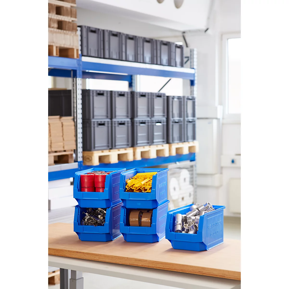 Contenedores de plástico azul llenos de varios artículos, frente a un estante de almacén.