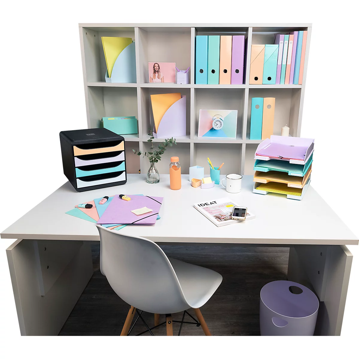 Bureau avec fournitures de bureau : bacs à courrier, dossiers, notes, stylos. Couleurs : pastel. Étagère en arrière-plan.