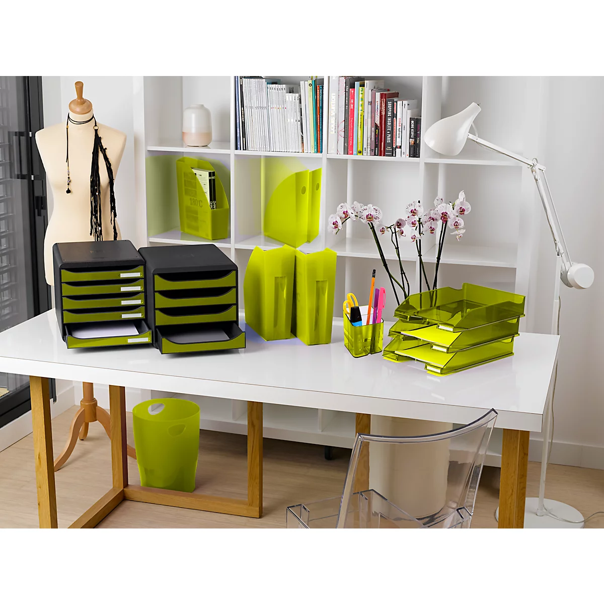 Bureau de bureau avec des plateaux de classement, des dossiers, un porte-stylos et des orchidées. Un portant et une étagère sont visibles en arrière-plan.