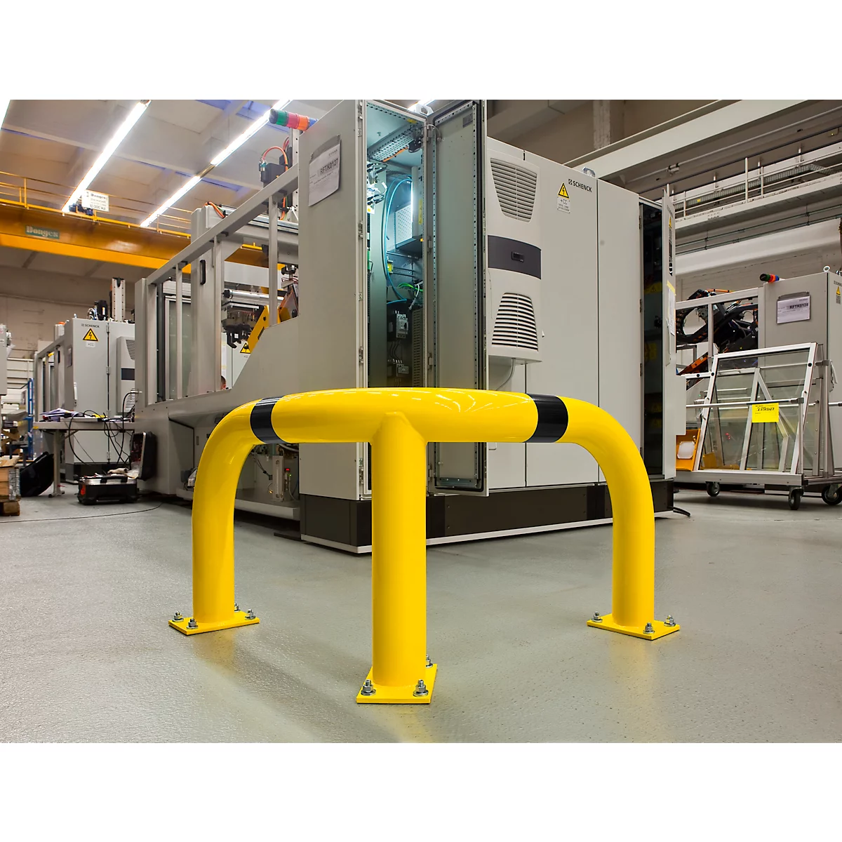 Yellow safety device for machines. Large plant in the background, open doors, factory hall.