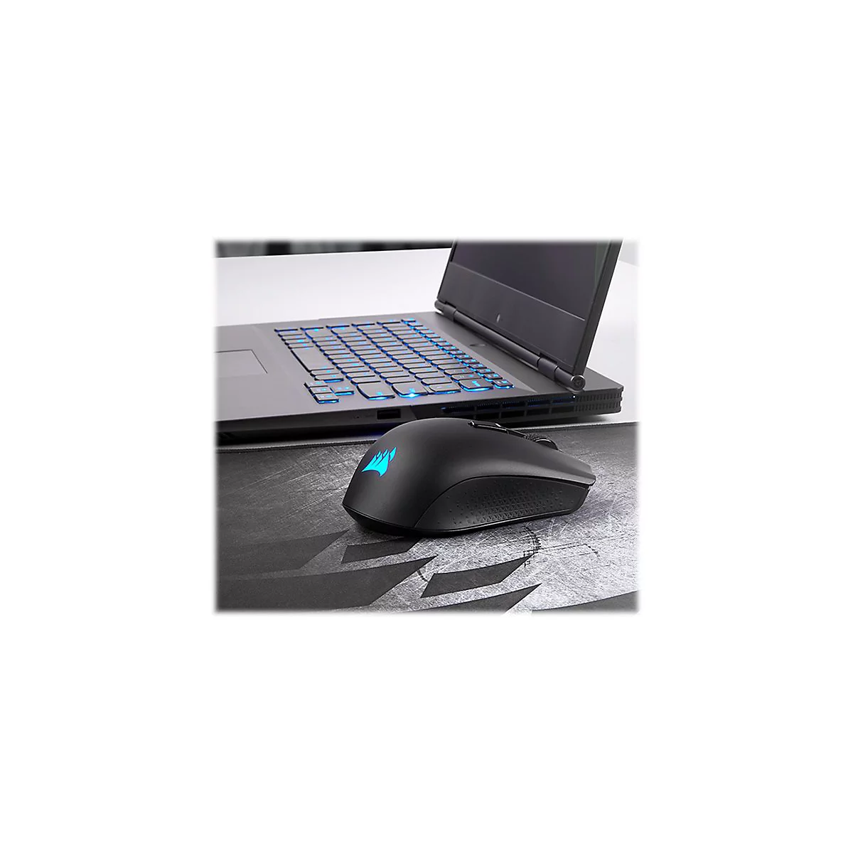 Schwarze Gaming-Maus mit leuchtendem Logo neben Laptop. Hintergrundgraue OberflÃ¤che und beleuchtete Tastatur.