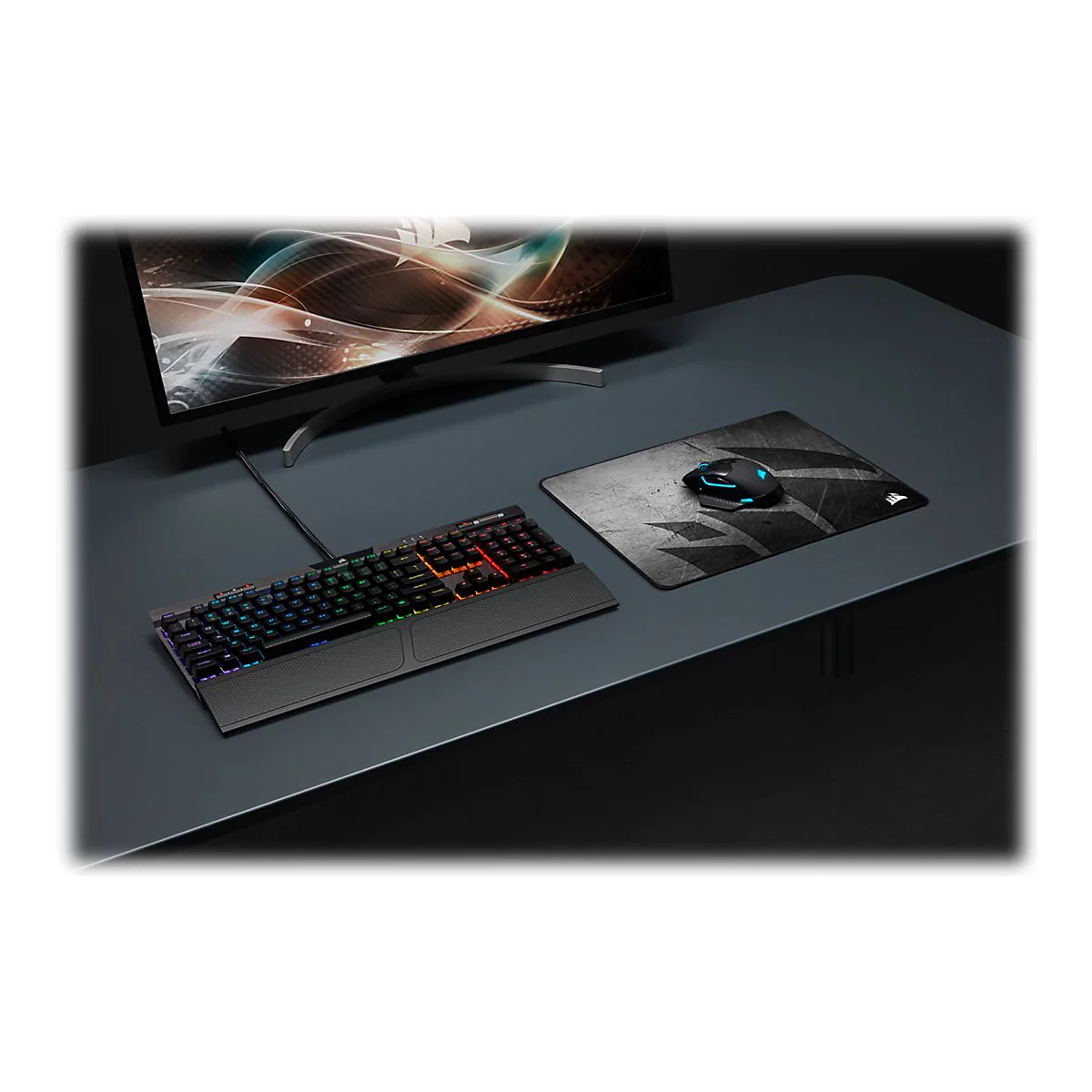 Ein Gaming-Setup mit beleuchteter Tastatur, Maus, Mauspad und Monitor auf einem dunklen Schreibtisch.