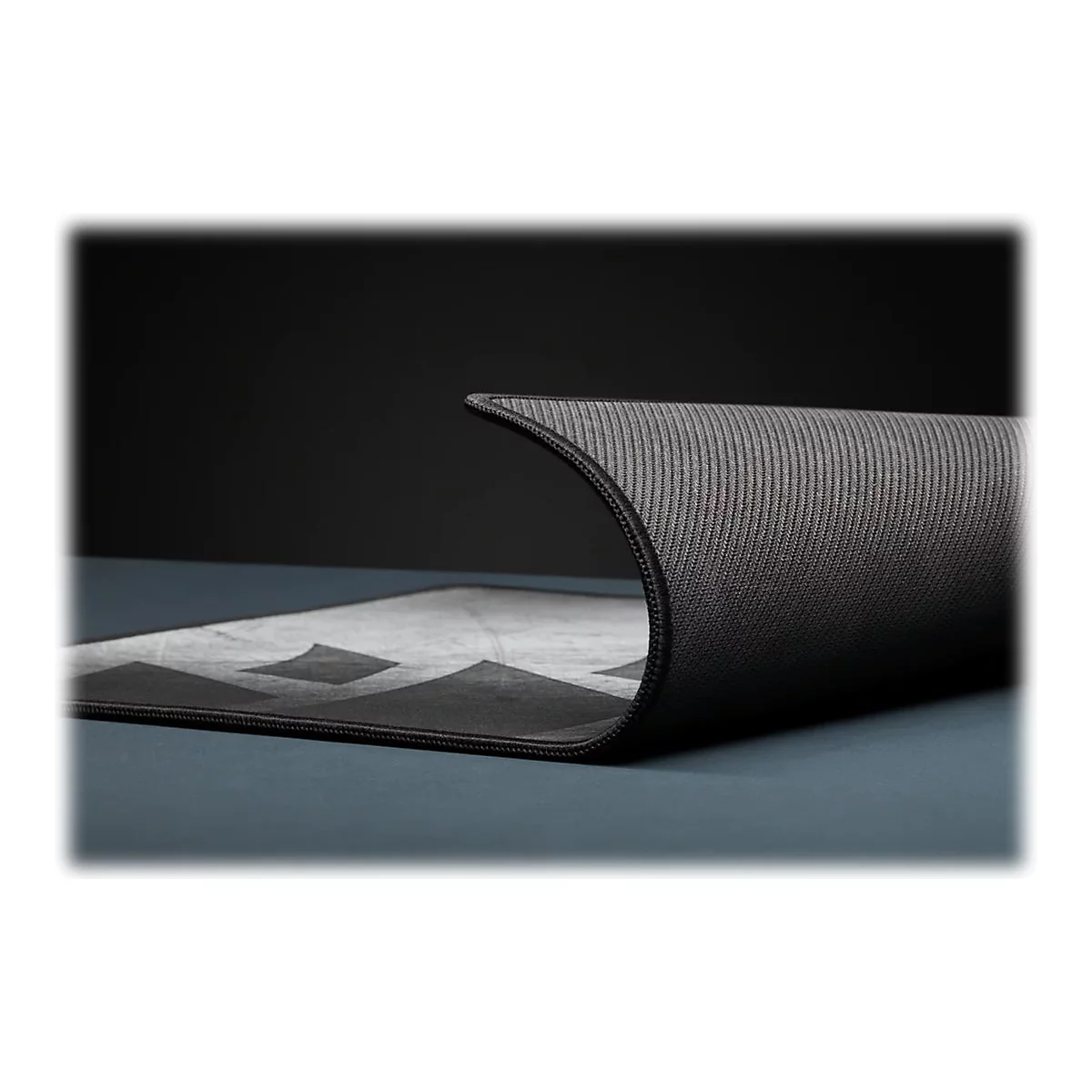 Detailaufnahme einer schwarzen Yogamatte, die sich an einer Ecke aufrollt. Auf der sichtbaren Seite ein geometrisches Muster.