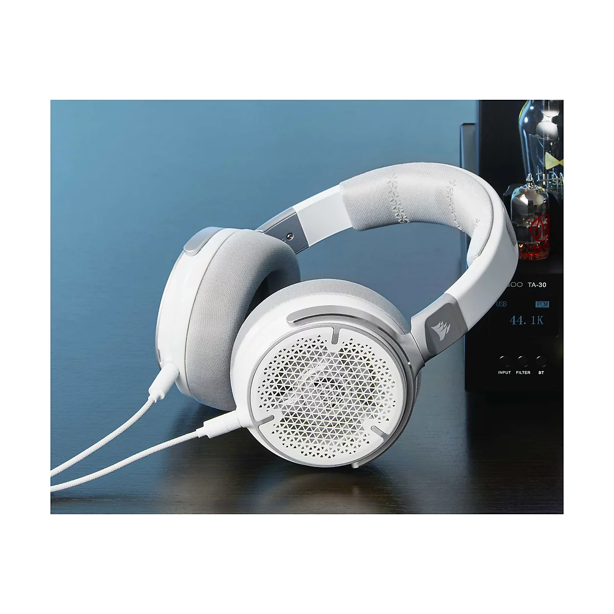 Weißes Gaming-Headset auf dunklem Holz. Der Bügel hat graue Details, die Ohrmuscheln sind ebenfalls grau. Auf einem schwarzen Gerät mit Display steht 44.1K.