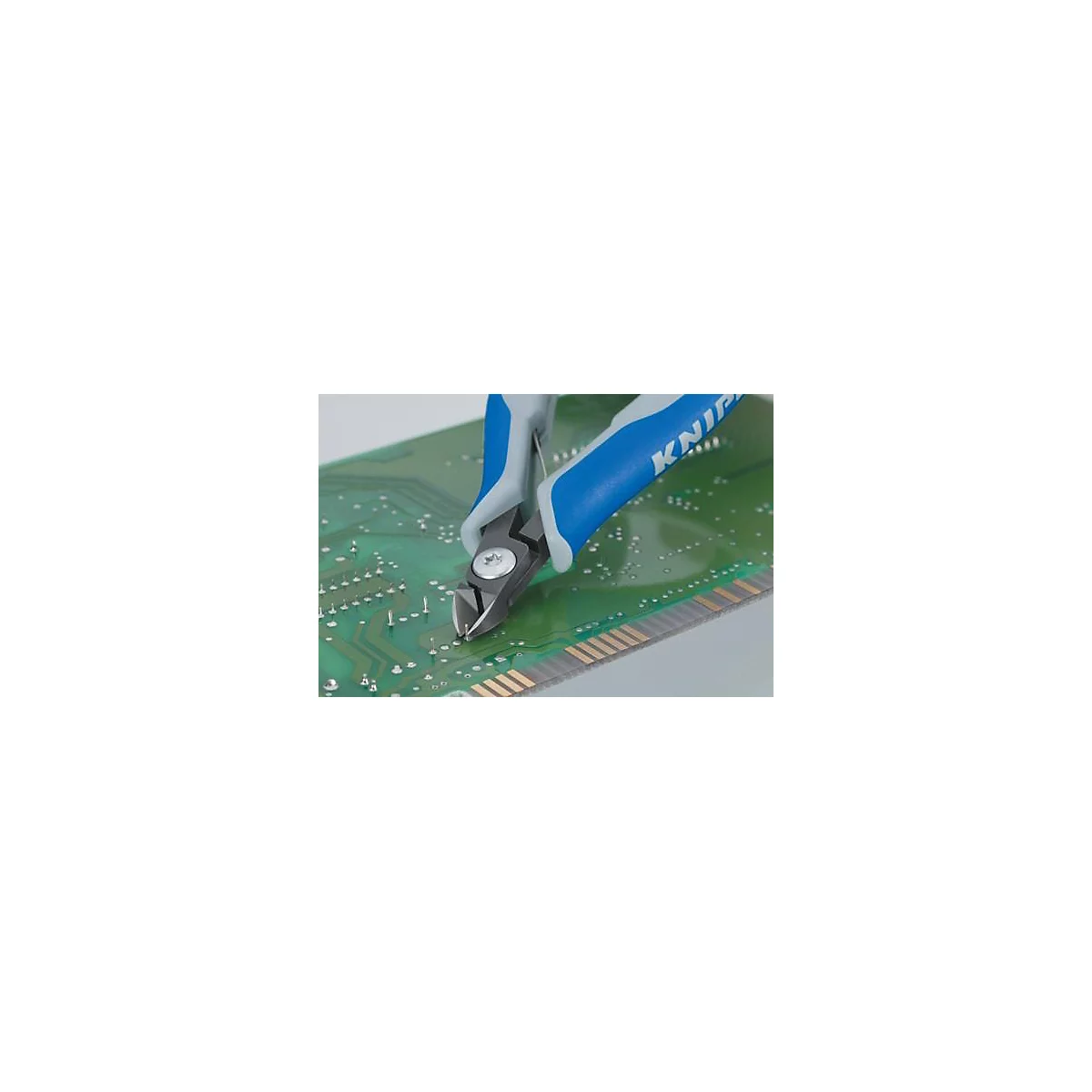 Des pinces coupantes bleues et grises coupent un fil sur une carte de circuit imprimé verte.