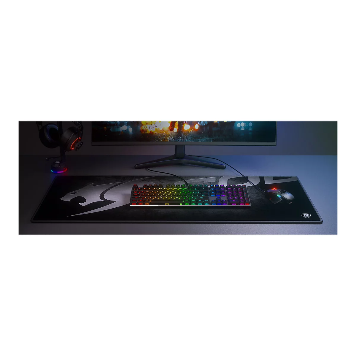 Draufsicht auf Gaming-Zubehör. Auf einem Schreibtisch liegen eine Tastatur, eine Maus und ein Mauspad. Links steht ein Kopfhörer. Auf dem Monitor wird ein Spiel gezeigt.