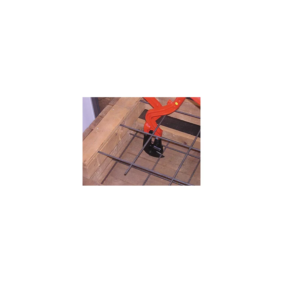 Gros plan : une pince à cintrer les barres d'armature orange saisit une grille de tiges métalliques.