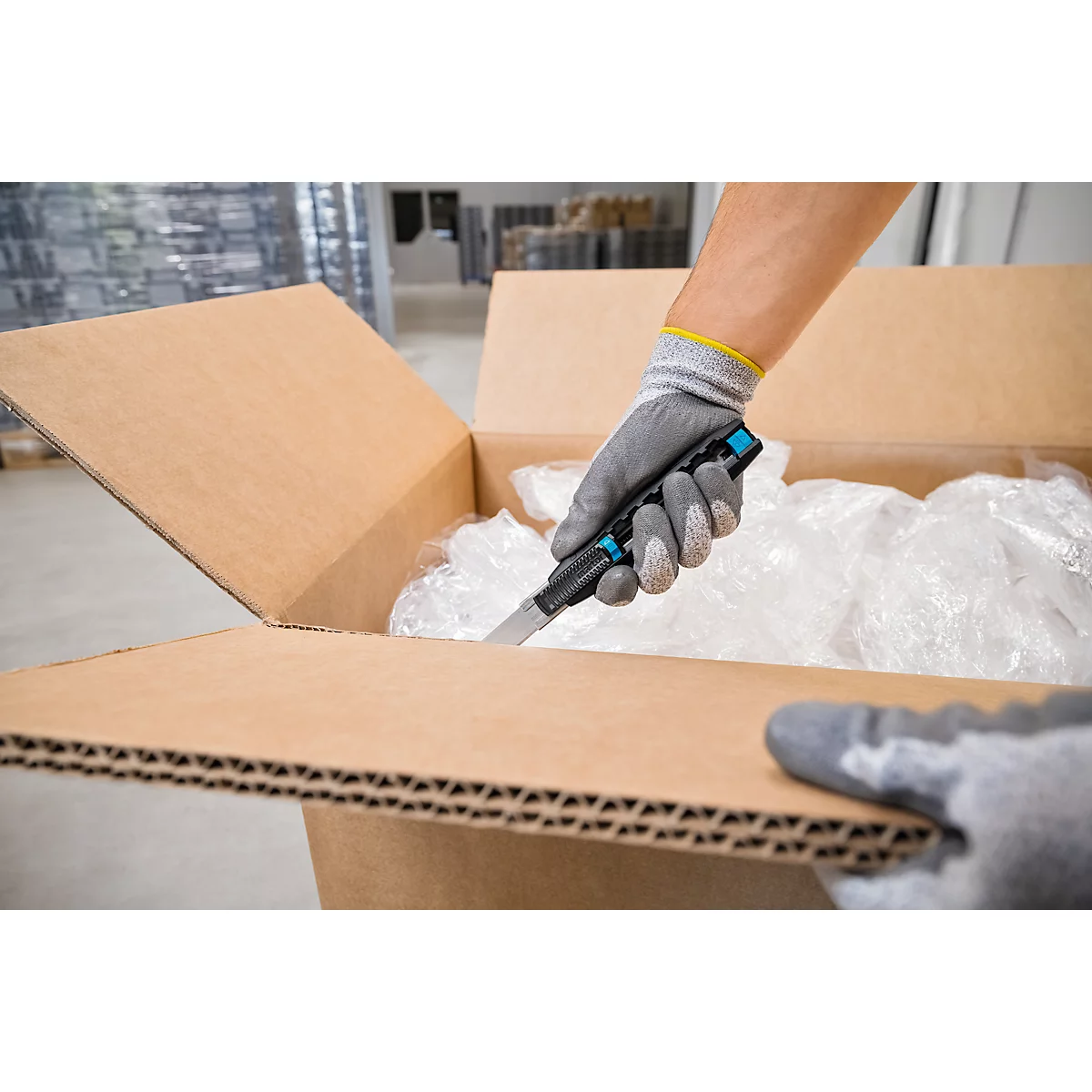 Personne coupant l'emballage avec un couteau. Les gants protègent les mains.