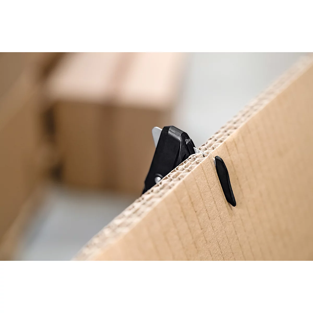 Un couteau de sécurité noir coupant à travers un morceau de carton ondulé épais.