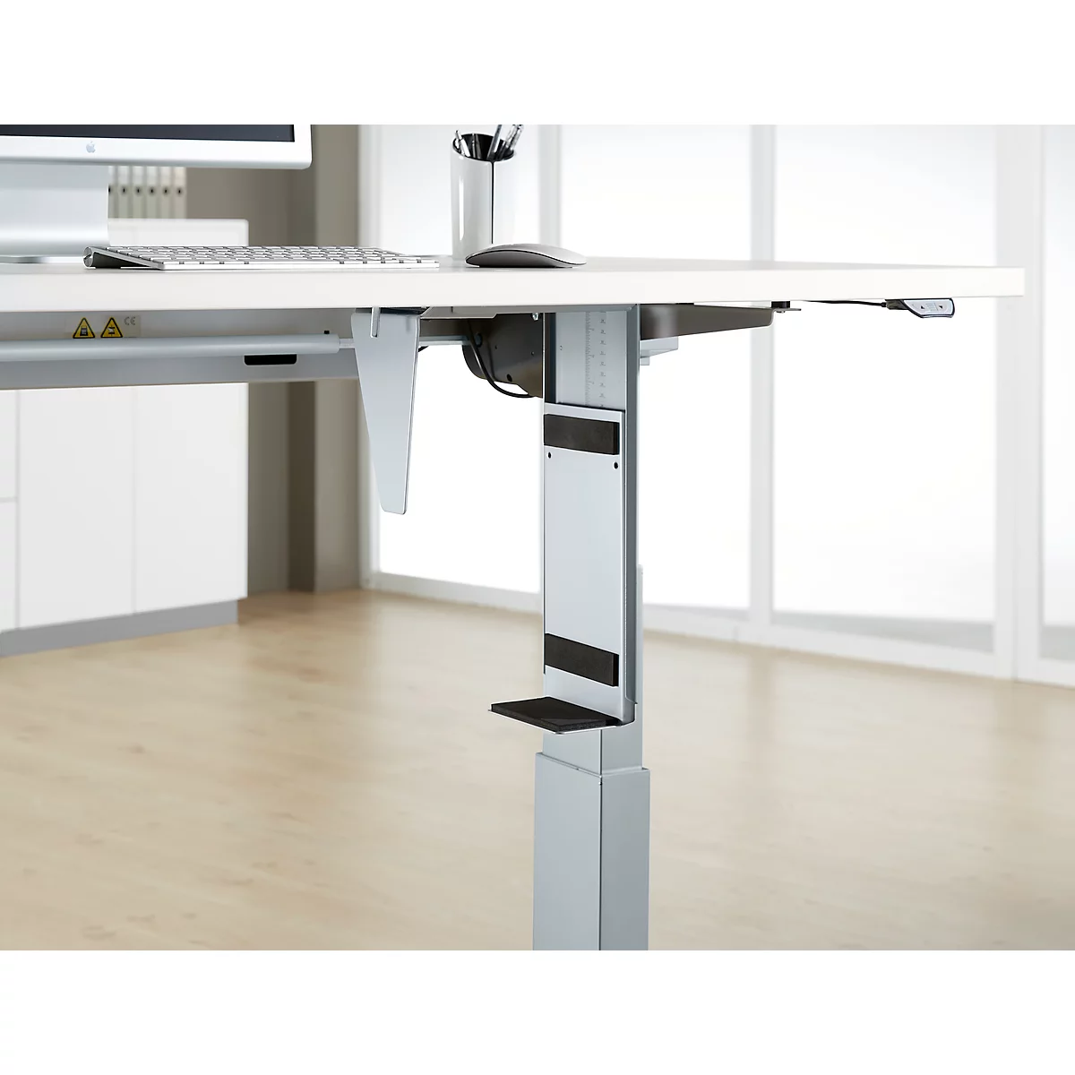 Close-up of a height-adjustable desk. The detail shows the silver frame, the black controls and the attachment.