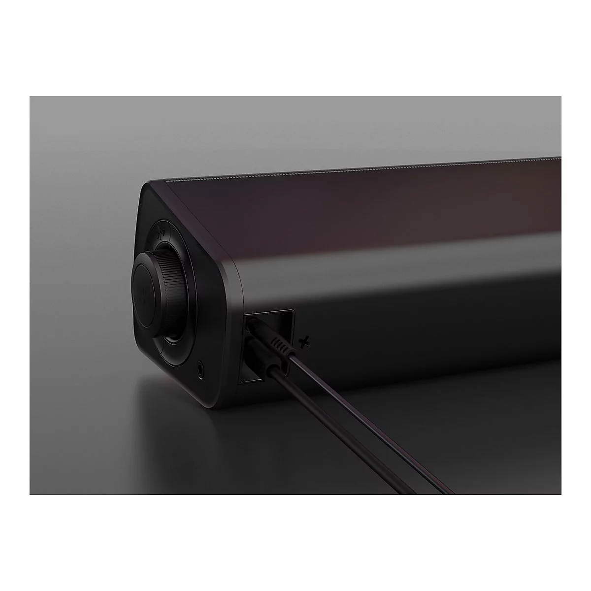 Nahaufnahme einer schwarzen Soundbar mit Drehknopf, Anschlüssen und Kabeln.