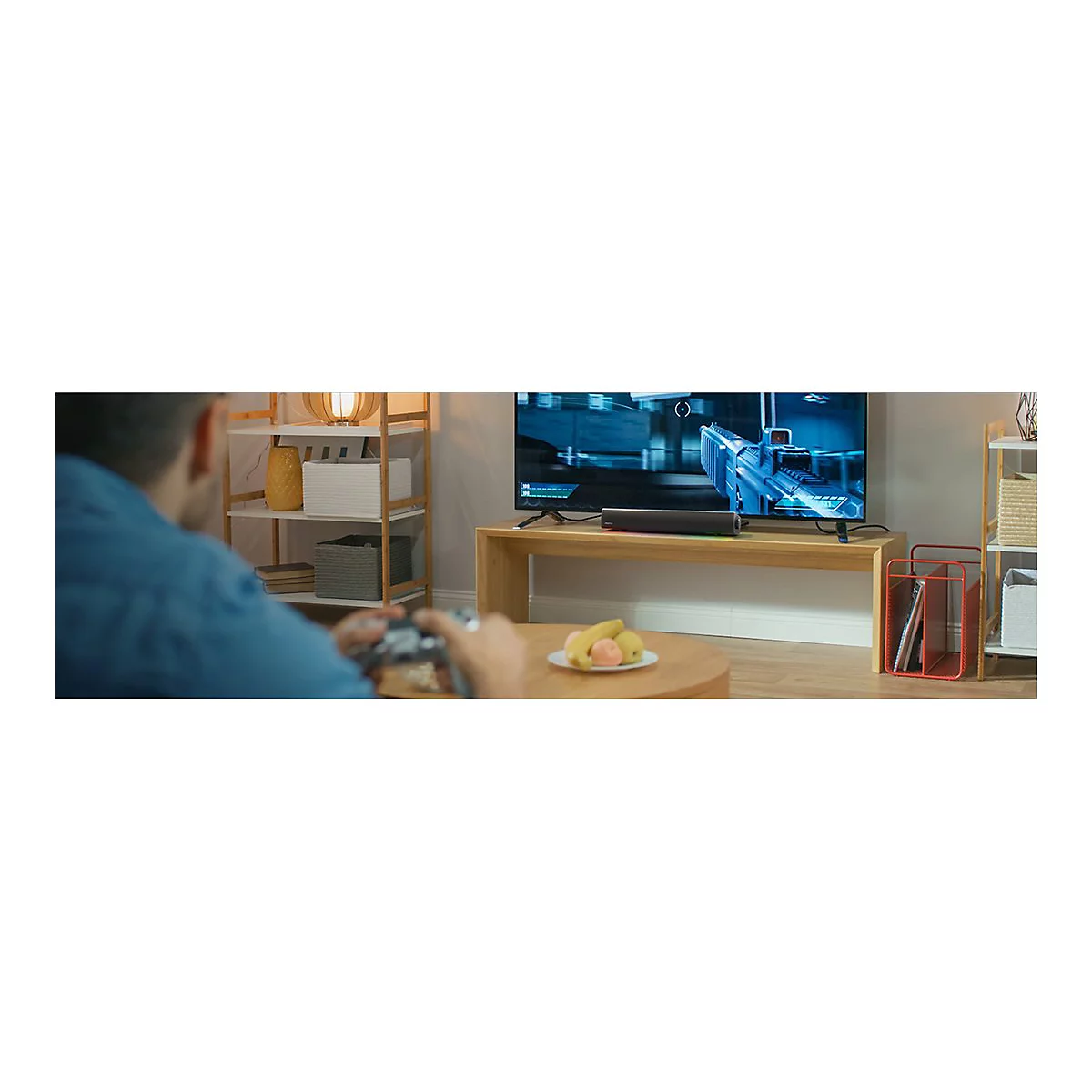 Mann spielt Videospiel auf einem großen Fernseher. Auf dem Tisch liegt Obst.