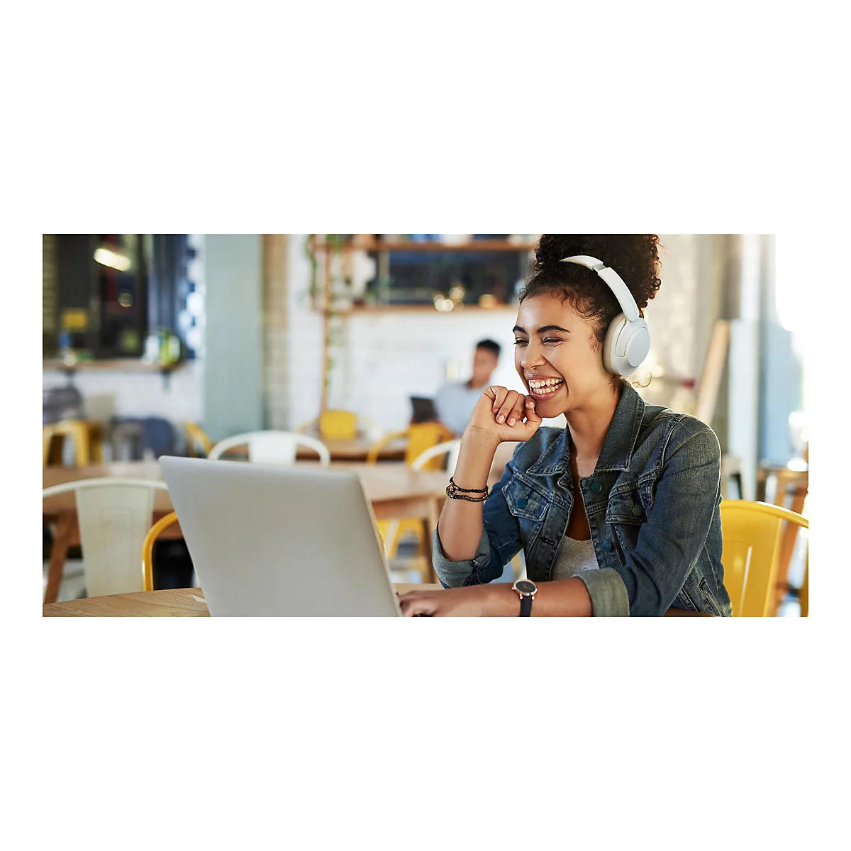 FrÃ¶hlich lÃ¤chelnde Frau mit KopfhÃ¶rern am Laptop im CafÃ©.