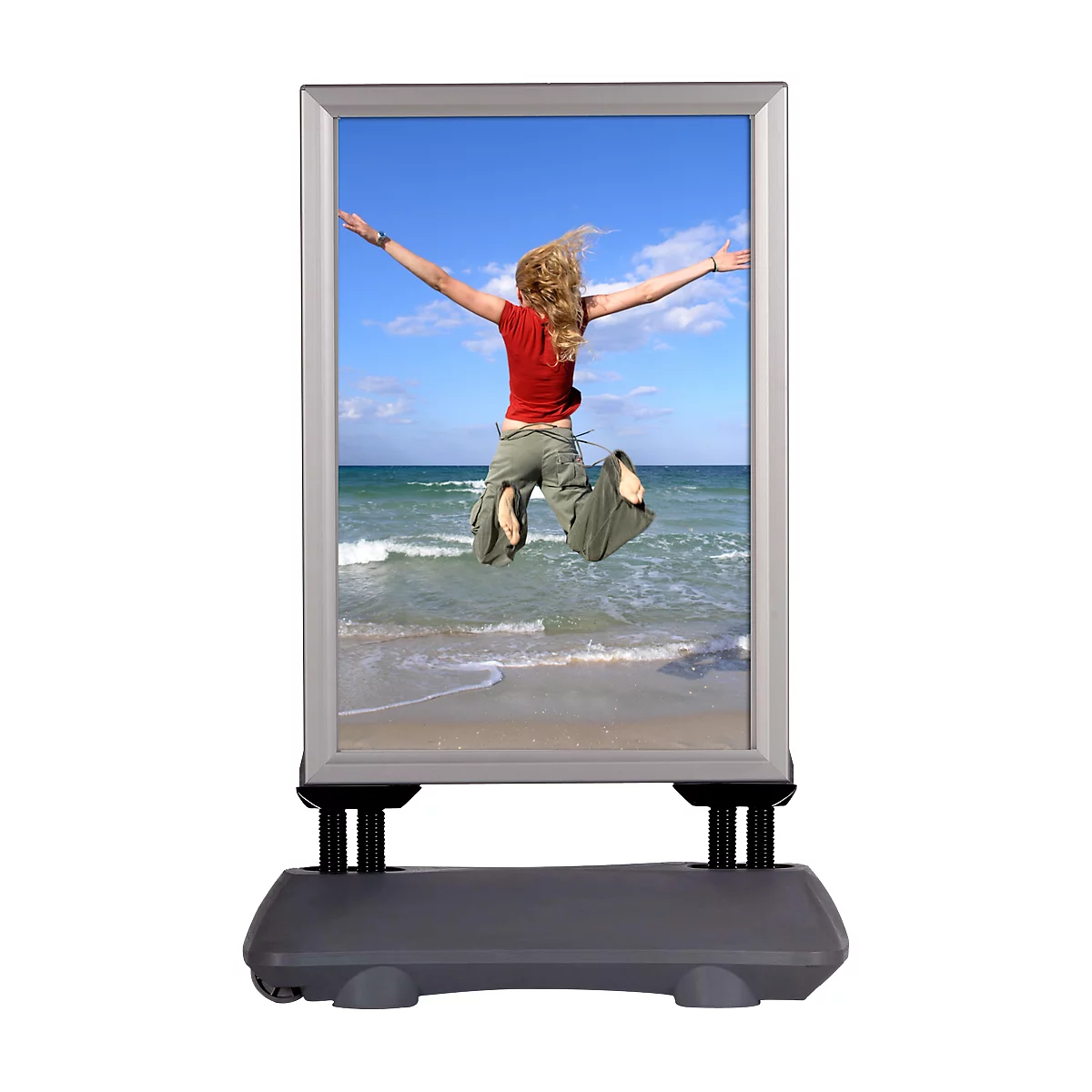 Advertising board showing a woman jumping on the beach. The board stands on a grey stand.