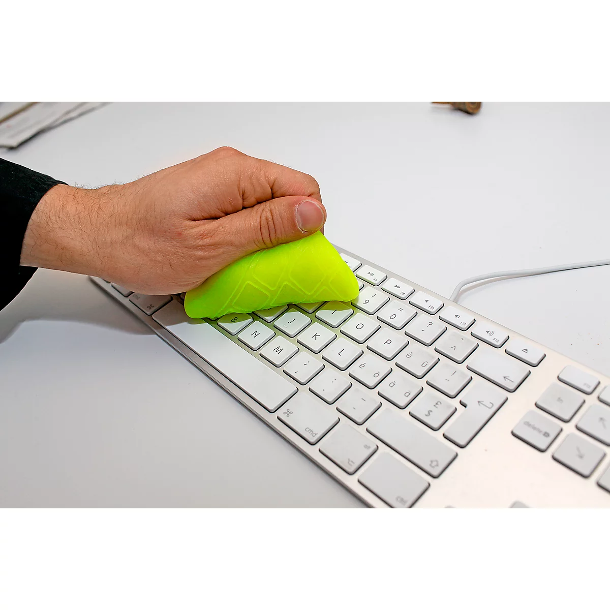 A hand cleans a white keyboard with a green sponge.
