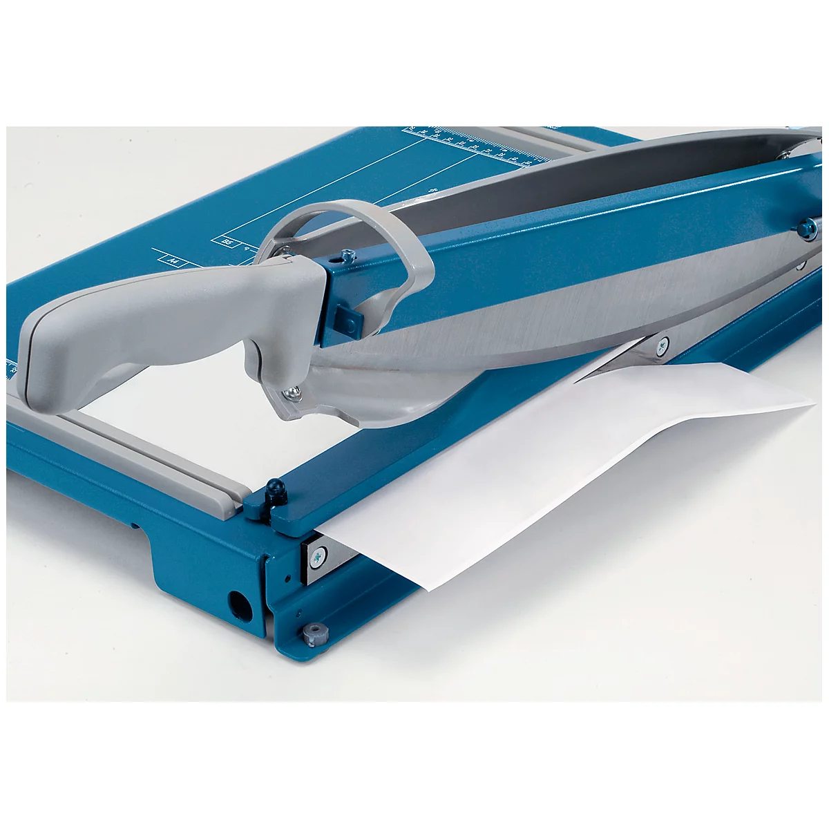 A blue and gray paper trimmer, with a white sheet of paper that is being cut.