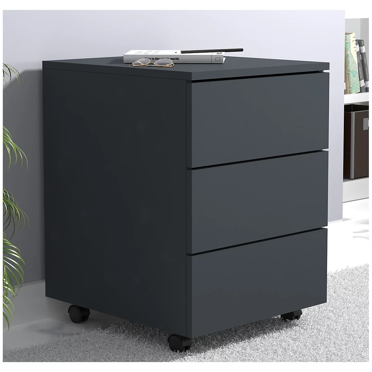 Dark gray rolling cabinet with three drawers and wheels. Glasses and a book are on top.