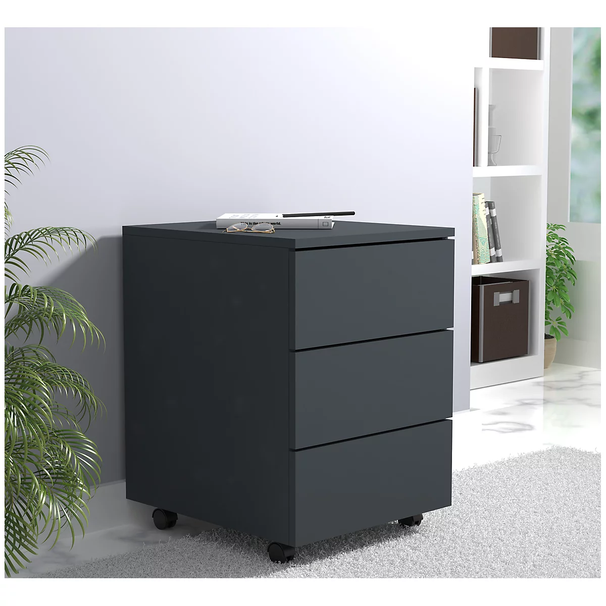 Dark gray filing cabinet with three drawers on wheels. Pens and glasses lie on top.