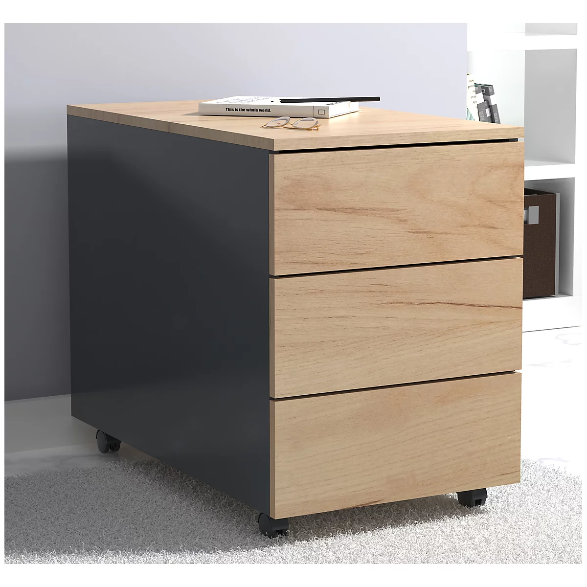 A gray rolling cabinet with three drawers. A book, glasses and a pen are on top.