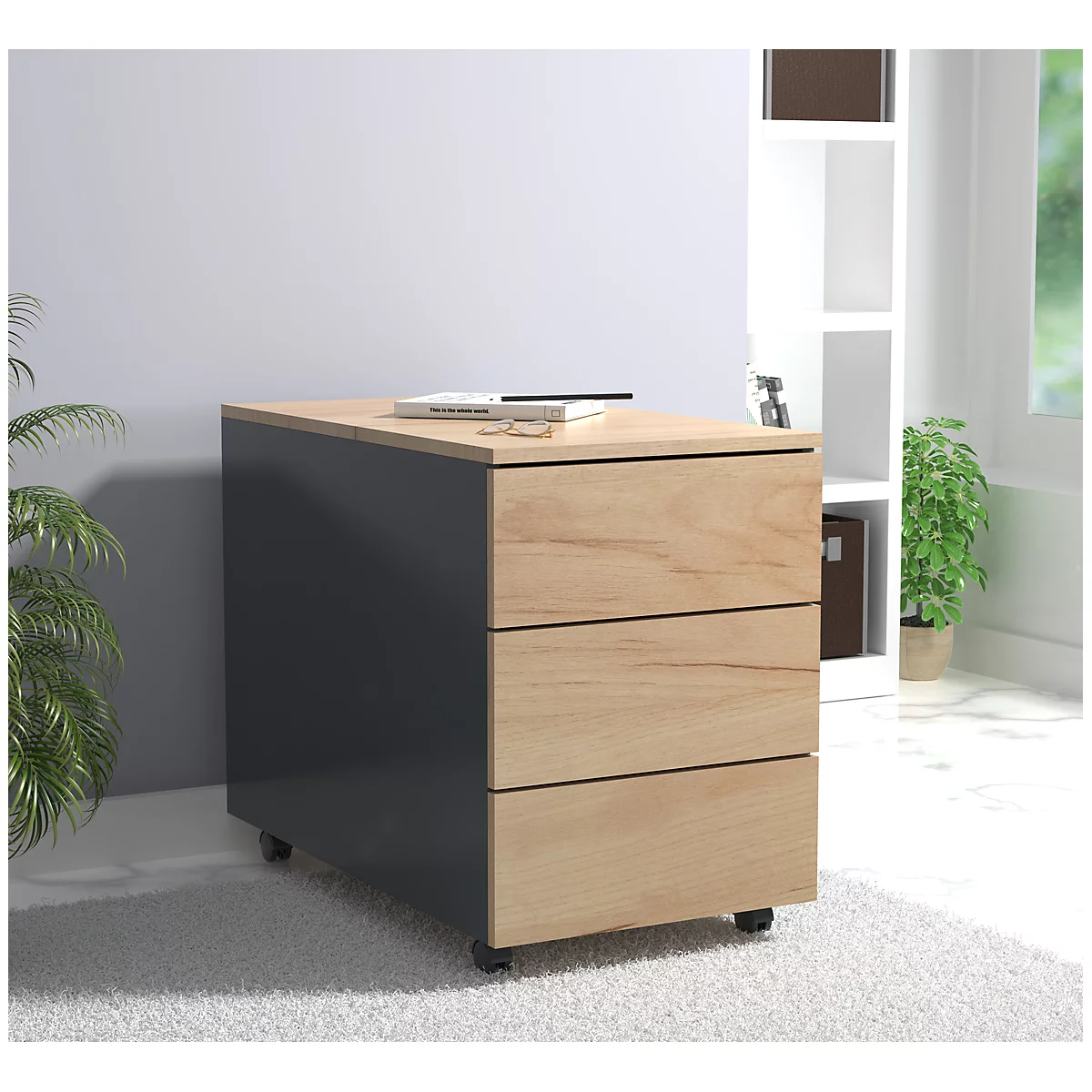 A gray rolling cabinet with three wooden drawers, a book and a pen are on top.
