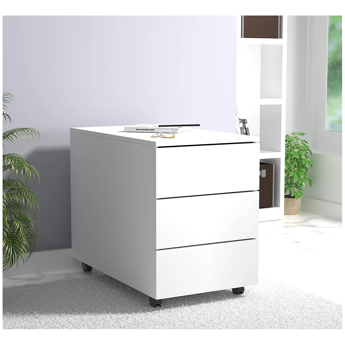 White rolling file cabinet with three drawers, on which rests a book, glasses, and other items. A bookcase can be seen behind it.