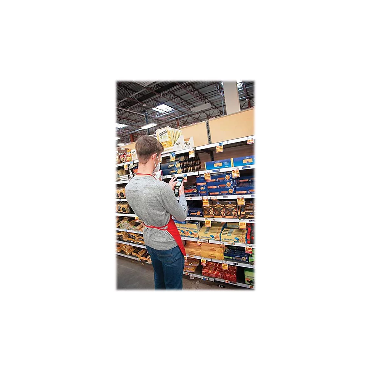 Ein Mann mit Maske scannt im Supermarkt Ware. Er trÃ¤gt eine rote SchÃ¼rze.