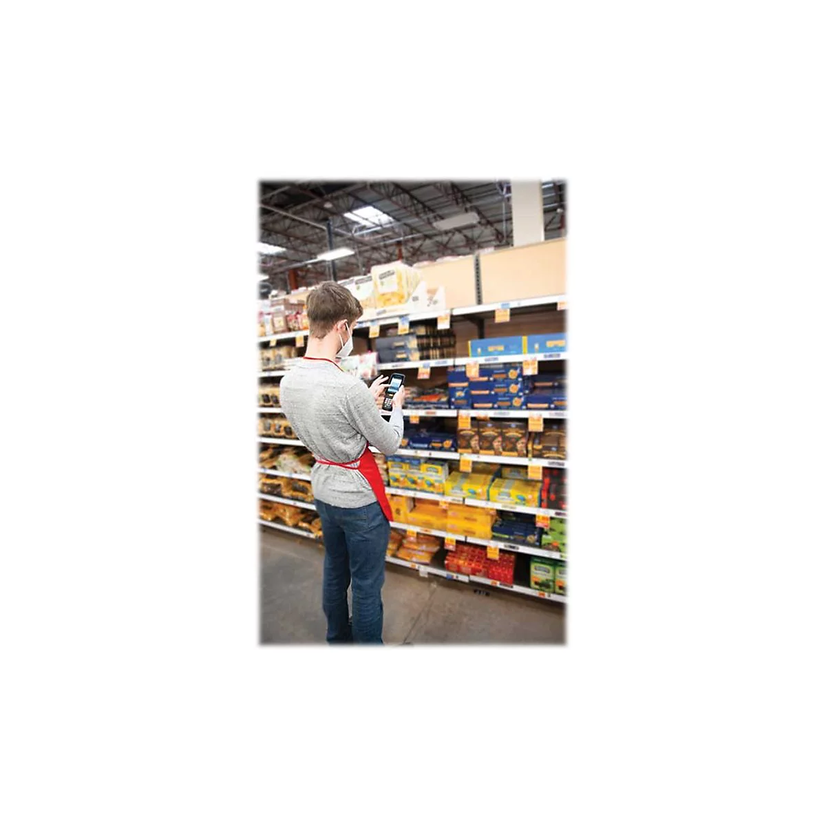 Ein Mann mit Mundschutz scannt im Supermarkt Waren. Er trÃ¤gt eine rote SchÃ¼rze.