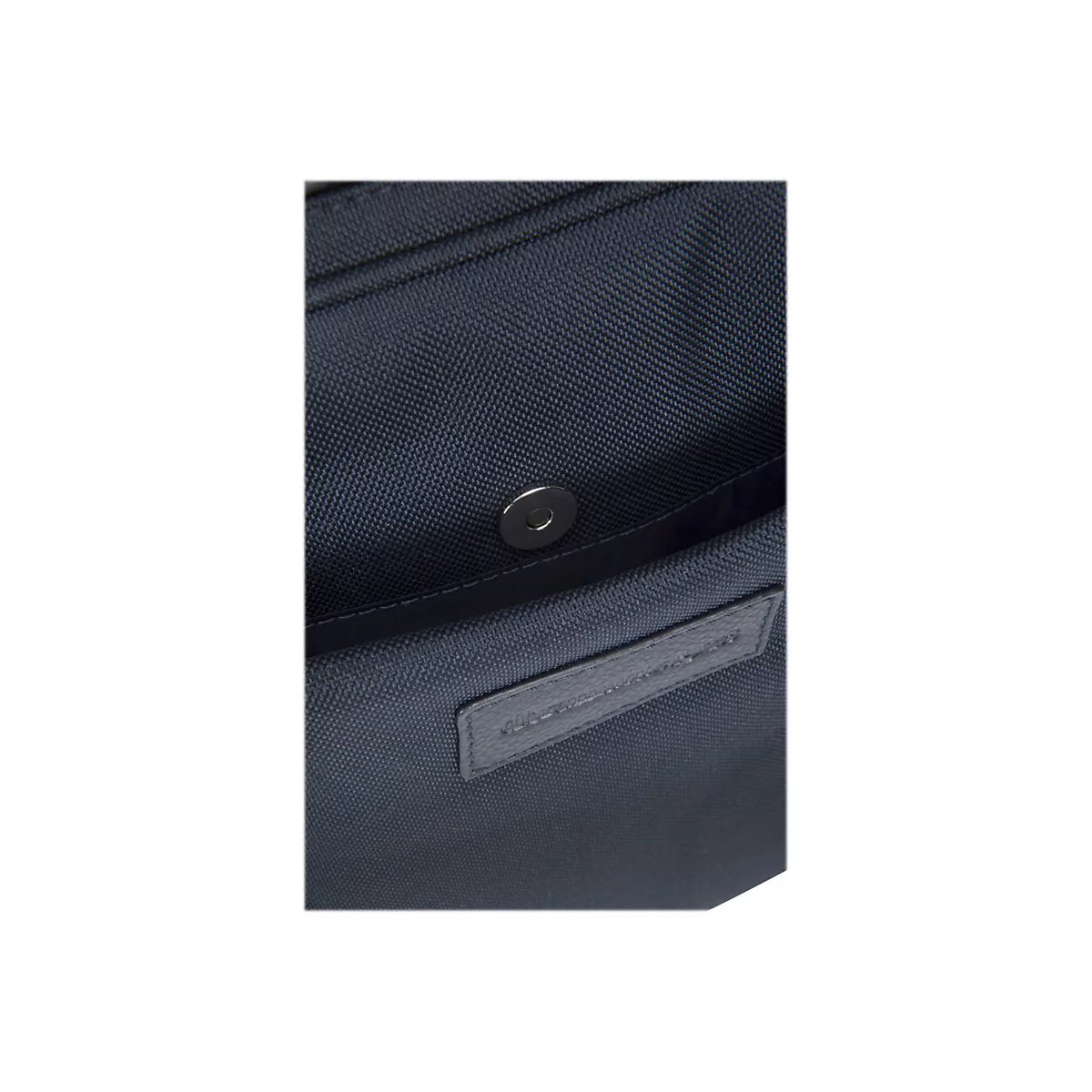 Detailaufnahme einer blauen Handtasche. Ein silberner Magnetverschluss und ein Lederetikett mit Schriftzug sind zu sehen.