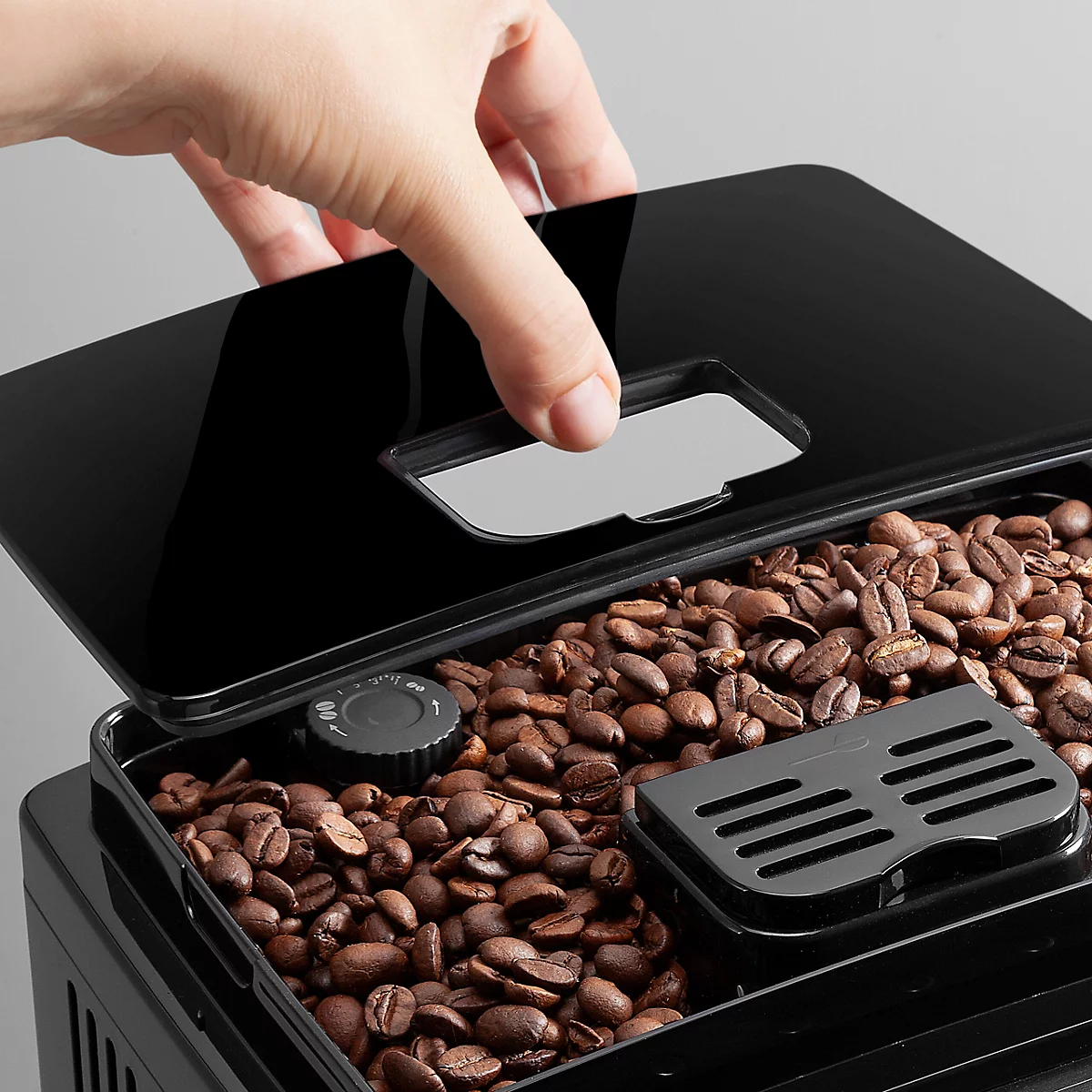 Hand öffnet Deckel eines Kaffeebehälters mit Kaffeebohnen. Schwarzer Deckel, Bohnen liegen im Behälter.