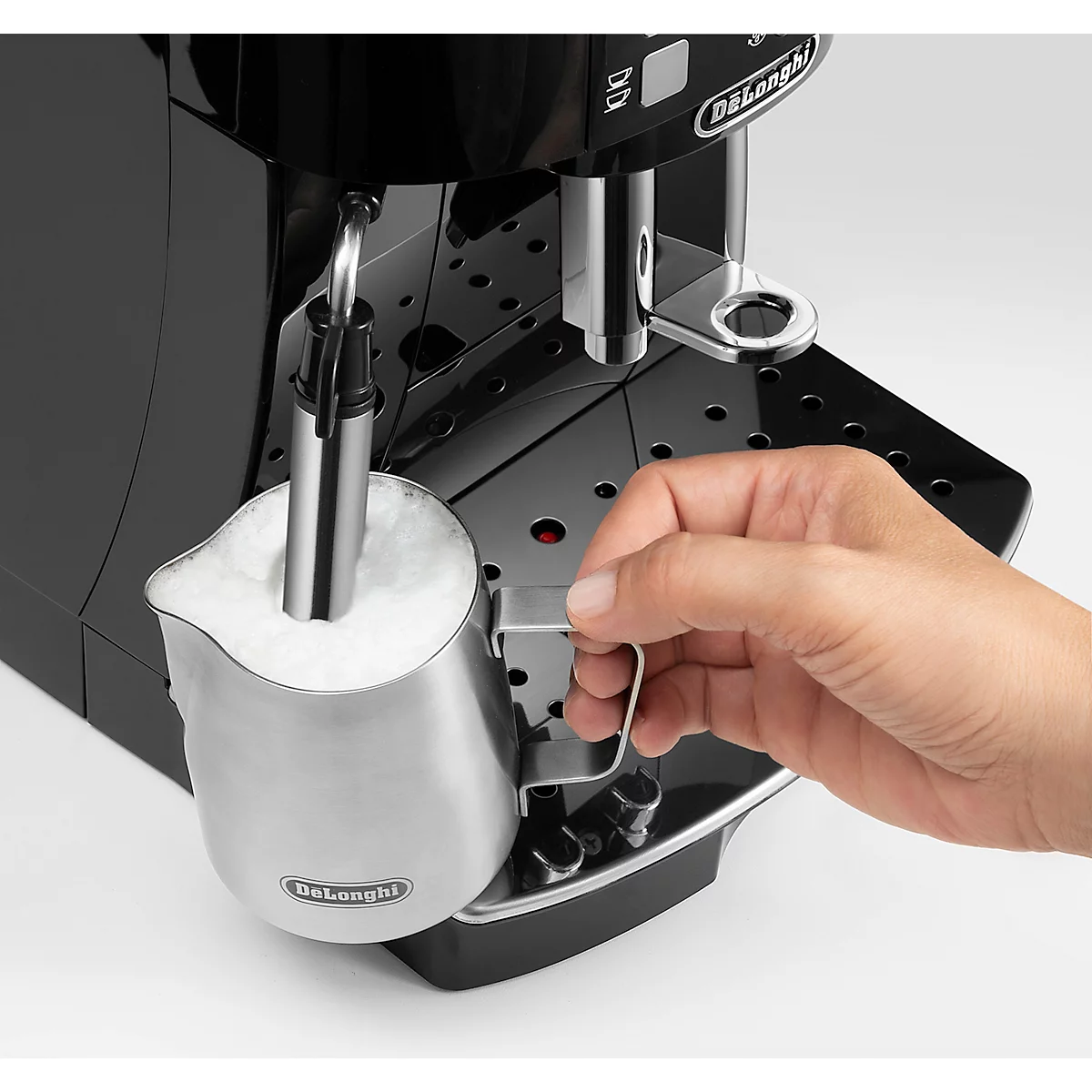 Nahaufnahme einer schwarzen Delonghi Espressomaschine. In der Milchschaumkanne wird mit der Dampfdüse Milch aufgeschäumt. Eine Hand hält die Kanne.