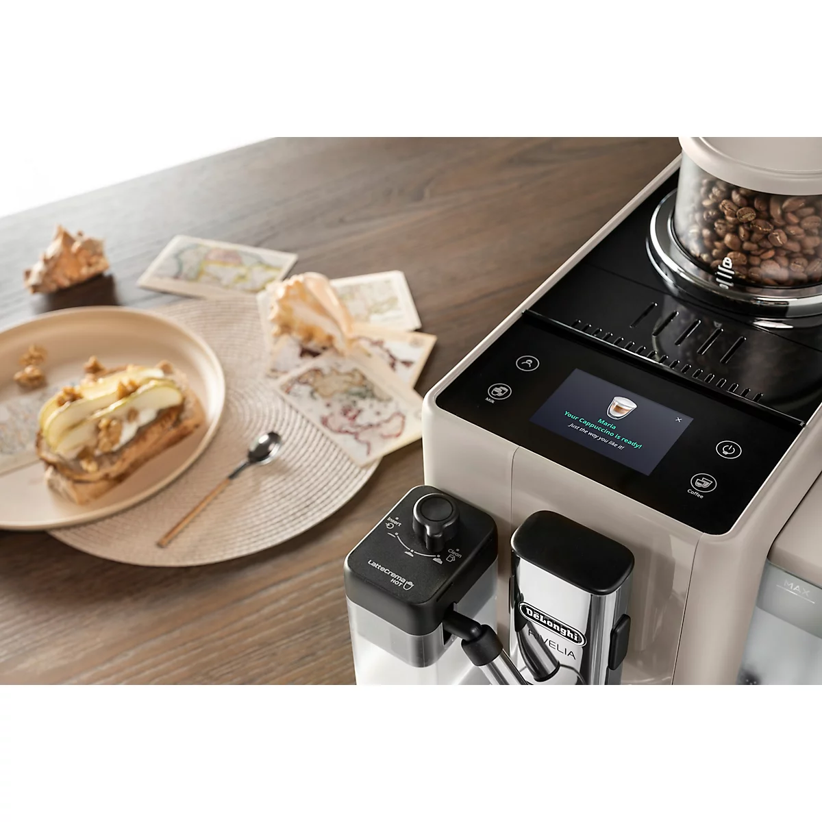 Kaffeemaschine, Kaffeezubereitung, Gebäck, Karten, Muscheln liegen auf einem Tisch. Das Display zeigt eine Kaffeetasse.