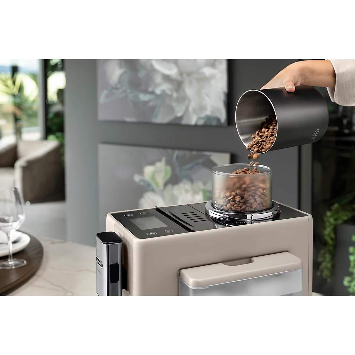 Kaffeebohnen werden in eine Kaffeemaschine gefüllt. Graue Kaffeemaschine auf einer hellen Arbeitsplatte.